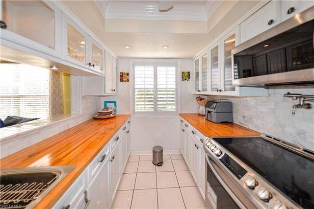 22161 Tallwood Ct, #706, Estero, FL 33928 Galley kitchen featuring white cabinetry, stainless steel appliances, wood-finish countertops, tiled flooring, and a window with plantation shutters