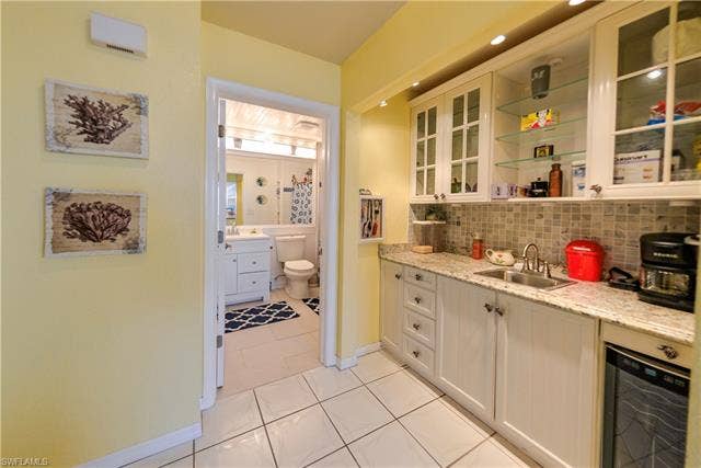 22161 Tallwood Ct, #706, Estero, FL 33928 White cabinetry with granite-style countertops, stainless steel sink, and mosaic tile backsplash