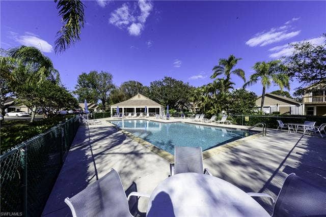 22161 Tallwood Ct, #706, Estero, FL 33928 Community swimming pool with a surrounding concrete deck, flanked by mature palm trees and lush greenery