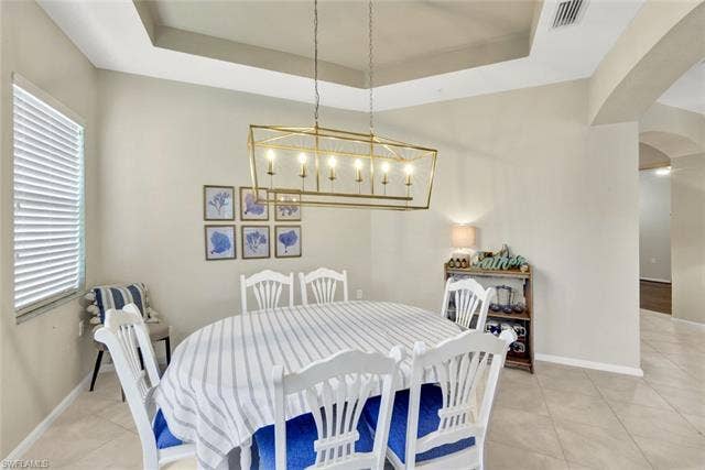 10060 Valiant Ct, #202, Miromar Lakes, FL 33913 Tray ceiling featuring a gold-finish linear chandelier, tile flooring, and a window with horizontal blinds
