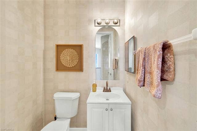 10060 Valiant Ct, #202, Miromar Lakes, FL 33913 Bathroom featuring a white vanity with integrated sink, bronze-finish faucet, and a wall-mounted arched mirror
