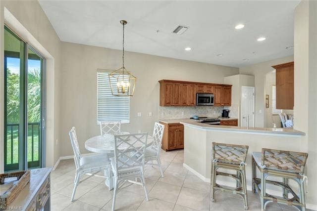 10060 Valiant Ct, #202, Miromar Lakes, FL 33913 Open-concept kitchen and dining area featuring wood cabinetry, stainless steel appliances, and a tiled backsplash