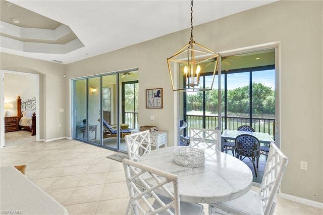 10060 Valiant Ct, #202, Miromar Lakes, FL 33913 Dining area featuring a contemporary gold-finish chandelier, tray ceiling, and tile flooring
