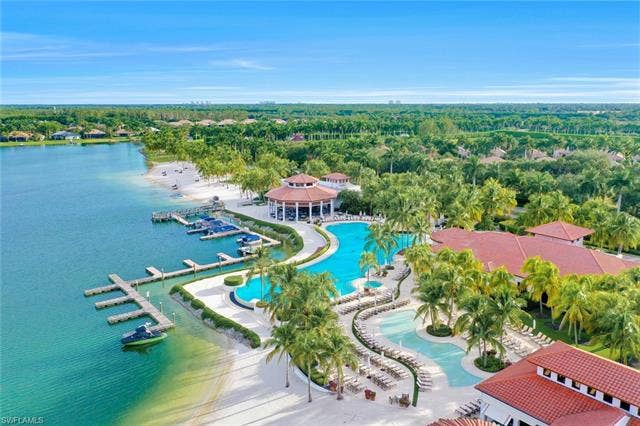 10060 Valiant Ct, #202, Miromar Lakes, FL 33913 Expansive resort-style pool complex featuring multiple swimming areas, a large central pavilion with a red tile roof, and extensive sun loungers