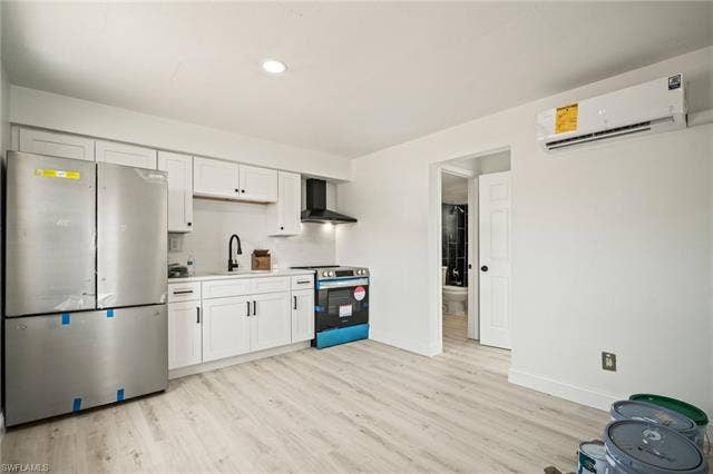 2316 Bayside St, Naples, FL 34112 Kitchen featuring stainless steel appliances, a wall mounted air conditioner, wall chimney range hood, light wood-type flooring, and backsplash