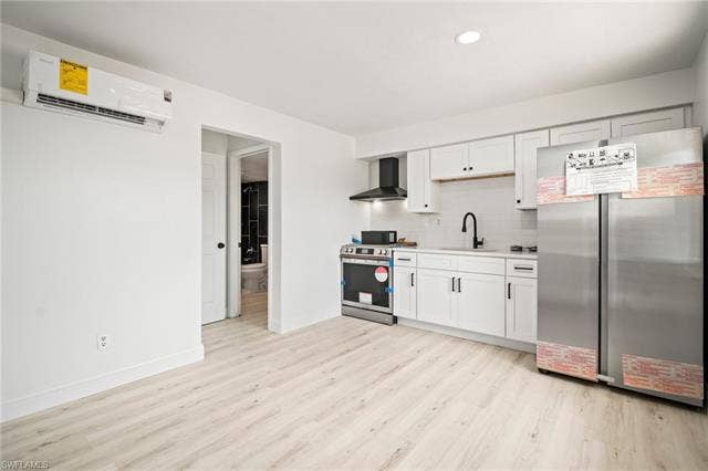 2316 Bayside St, Naples, FL 34112 Kitchen featuring stainless steel appliances, wall chimney exhaust hood, a wall mounted AC, light wood-style flooring, and light countertops