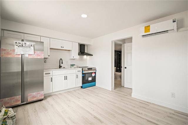 2316 Bayside St, Naples, FL 34112 Kitchen with appliances with stainless steel finishes, wall chimney exhaust hood, an AC wall unit, light countertops, and light wood-style floors