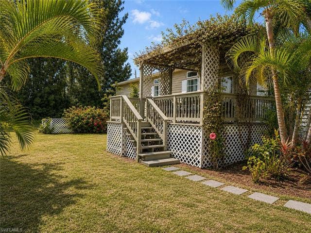 20472 Luettich Ln, Estero, FL 33928 Raised deck with lattice skirting, wood pergola with climbing vines, and tropical landscaping