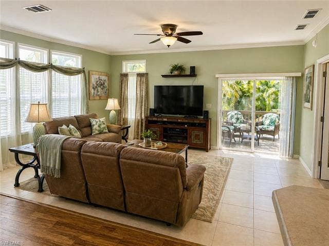 20472 Luettich Ln, Estero, FL 33928 Spacious living area featuring light-toned tile flooring, an integrated ceiling fan with lighting, and multiple windows with white blinds