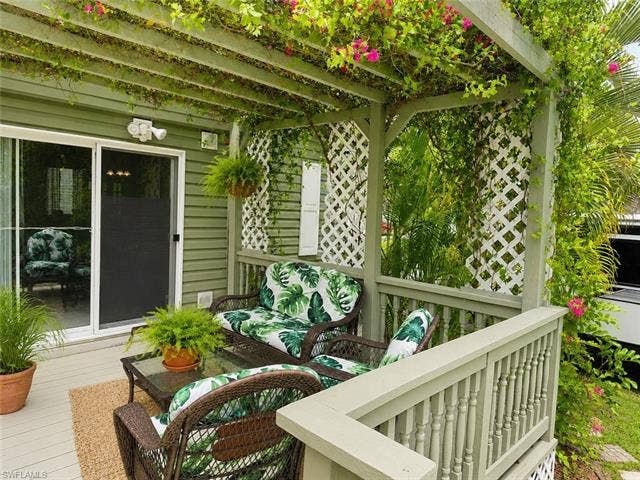 20472 Luettich Ln, Estero, FL 33928 Outdoor patio featuring a pergola with mature vines and pink blossoms, wood-finish decking, and white lattice panels