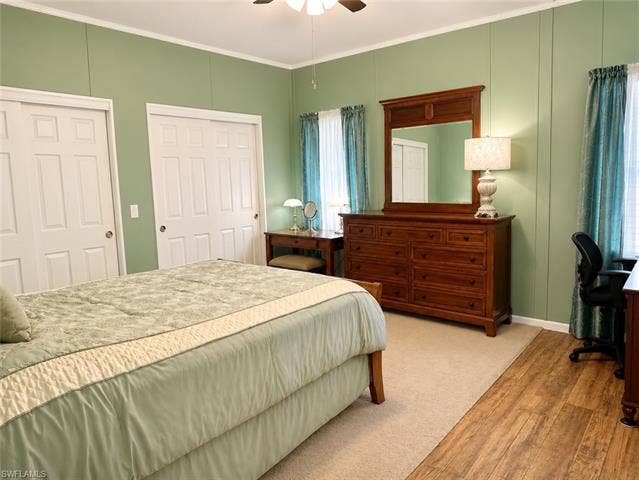 20472 Luettich Ln, Estero, FL 33928 Bedroom featuring a ceiling fan, two white paneled sliding closet doors, and wood-finish flooring extending into the space