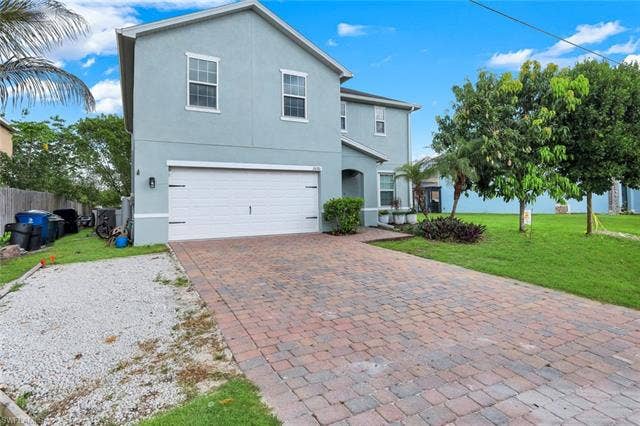 26701 Lincoln Ave, Bonita Springs, FL 34135 Two-story stucco exterior featuring a two-car garage with a white door, a paved driveway, and established landscape plantings