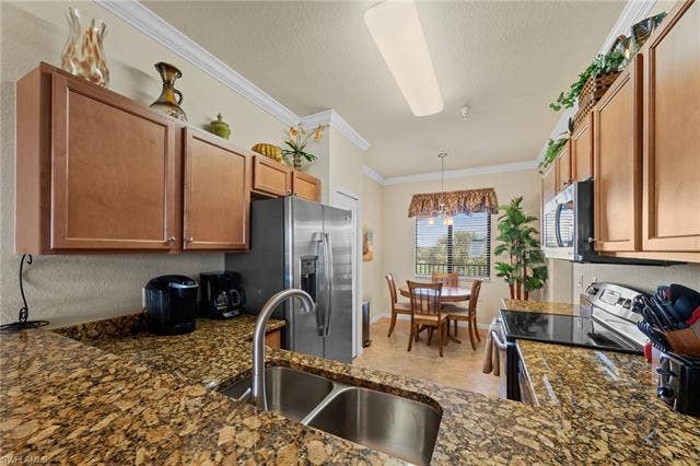17921 Bonita National Blvd, #244, Bonita Springs, FL 34135 Kitchen featuring a double stainless steel sink, patterned stone countertops, wood-finish cabinetry, and stainless steel appliances