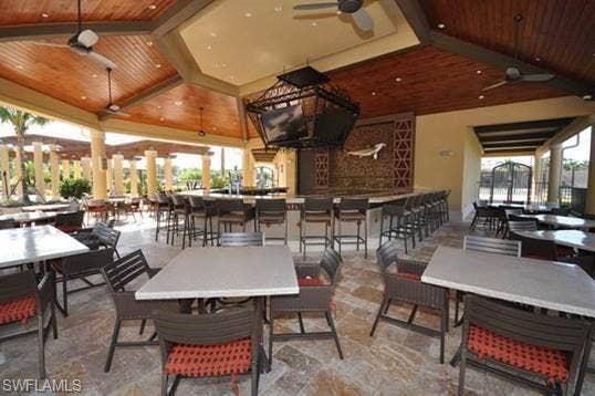 17921 Bonita National Blvd, #244, Bonita Springs, FL 34135 Expansive outdoor covered patio featuring a full-service bar with bar seating, multiple dining tables, wood-paneled ceilings with ceiling fans, and stone-finish flooring