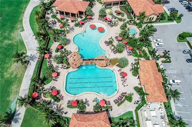 17921 Bonita National Blvd, #244, Bonita Springs, FL 34135 Expansive resort-style pool complex featuring two distinct swimming pools, a rock-detailed bridge, and multiple red-umbrella shaded lounge areas