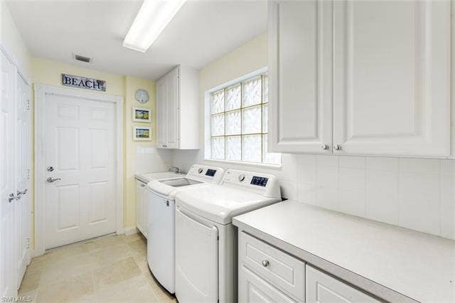 28179 Islet Trl, Bonita Springs, FL 34135 Dedicated utility space featuring ample white cabinetry, a glass block window, light-toned flooring, and a countertop with storage below