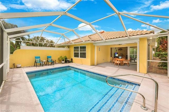 28179 Islet Trl, Bonita Springs, FL 34135 Screened-in pool area featuring a rectangular swimming pool with integrated steps and handrail, a spacious concrete paver deck, and a yellow stucco exterior