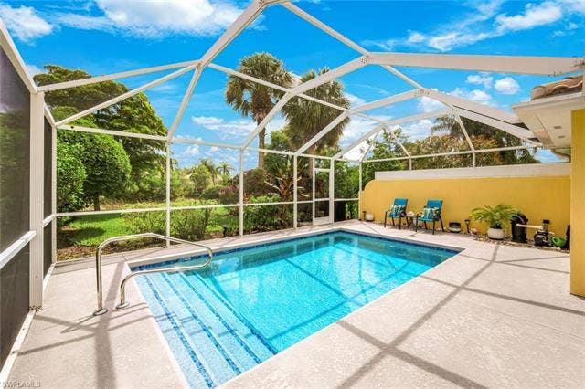 28179 Islet Trl, Bonita Springs, FL 34135 Screened outdoor pool area featuring a blue-tiled swimming pool with integrated steps, a surrounding concrete deck, and lush perimeter landscaping