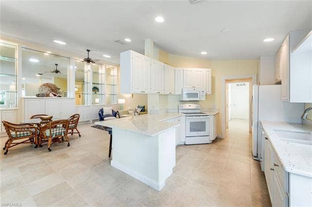 28179 Islet Trl, Bonita Springs, FL 34135 Spacious open-concept kitchen and living area featuring light-toned tile flooring, white cabinetry, integrated appliances, and light-colored countertops