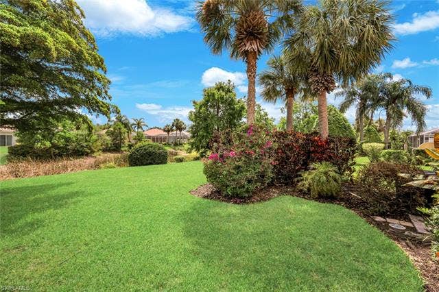 28179 Islet Trl, Bonita Springs, FL 34135 Expansive green lawn with established landscaping, including multiple palm trees and flowering shrubs