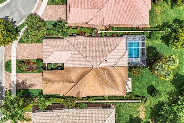 28179 Islet Trl, Bonita Springs, FL 34135 Tile roof residence featuring a screened pool enclosure, lush green landscaping, mature trees, and a paver driveway