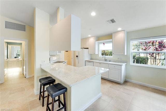 28179 Islet Trl, Bonita Springs, FL 34135 Open-concept kitchen featuring an island with a breakfast bar, white cabinetry, a built-in range, and a dual-basin sink under a window