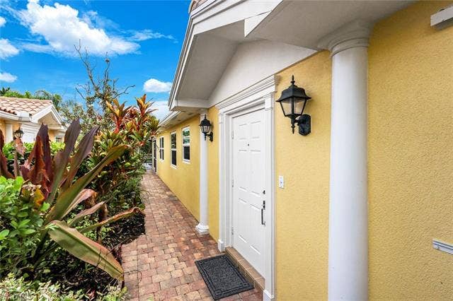 28179 Islet Trl, Bonita Springs, FL 34135 Front entry with a white paneled door, flanked by decorative columns and a wall-mounted lantern light fixture