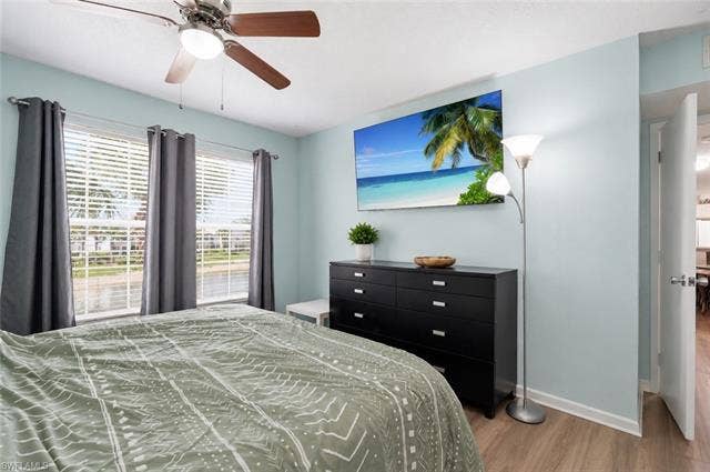 132 Santa Clara Dr, #10, Naples, FL 34104 Wood-finish flooring, two large windows with blinds, and a ceiling fan with integrated lighting