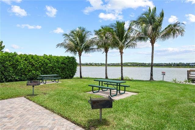 16112 Bonita Landing Cir, Bonita Springs, FL 34135 Grassy outdoor area featuring multiple picnic tables, two barbecue grills, and mature palm trees
