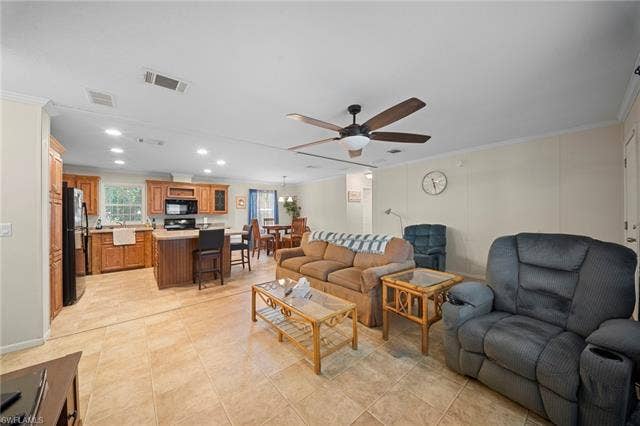 27472 Rue Viauv Ave, Bonita Springs, FL 34135 Open concept living area with tile flooring throughout, featuring a kitchen with wood cabinetry and black appliances, a dining area, and a living room with a ceiling fan