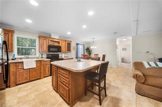 27472 Rue Viauv Ave, Bonita Springs, FL 34135 Open-concept kitchen featuring wood cabinetry, stone-finish countertops, black appliances, a central island with seating, and tile flooring