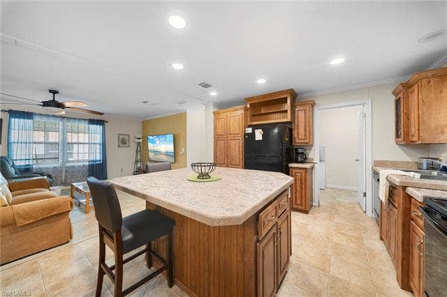 27472 Rue Viauv Ave, Bonita Springs, FL 34135 Kitchen featuring a central island with countertop seating, wood-finish cabinetry, black appliances, and tile flooring