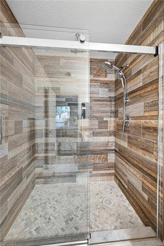 23461 Alamanda Dr, #206, Estero, FL 34135 Glass-enclosed shower featuring wood-finish wall tile and a mosaic tile floor