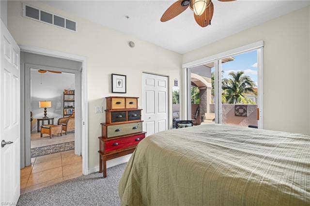 23461 Alamanda Dr, #206, Estero, FL 34135 Carpeted bedroom featuring a ceiling fan with integrated lighting, sliding glass doors opening to a private patio, and a separate doorway leading to a tiled interior space