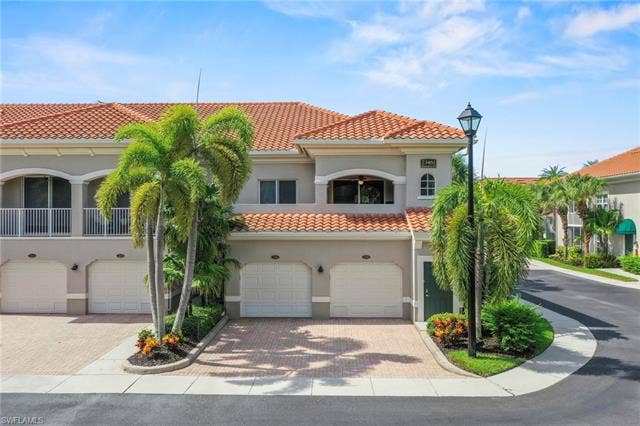23461 Alamanda Dr, #206, Estero, FL 34135 Mediterranean-inspired exterior featuring a terracotta tile roof, multiple garage bays, and a second-story balcony with white railings