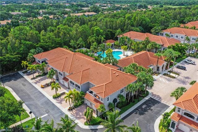 23461 Alamanda Dr, #206, Estero, FL 34135 Residential complex featuring multiple buildings with terracotta-style tile roofs, a central swimming pool with surrounding lounge areas, and paved parking facilities