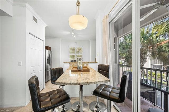 23461 Alamanda Dr, #206, Estero, FL 34135 Kitchenette featuring a granite-look breakfast bar with pendant lighting, stainless steel refrigerator, and tiled flooring