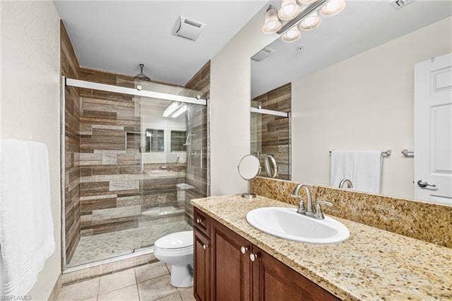 23461 Alamanda Dr, #206, Estero, FL 34135 Bathroom featuring a wood-finish tile shower with clear glass sliding doors, a built-in shower niche, and a rain showerhead