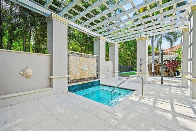 23461 Alamanda Dr, #206, Estero, FL 34135 Spa area featuring a tiled water feature, a white pergola, and light-toned paving