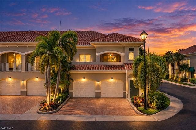 23461 Alamanda Dr, #206, Estero, FL 34135 Mediterranean-style architecture with a tile roof, multiple attached garages, a private balcony, palm trees, and brick paver driveways
