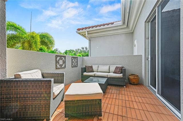 23461 Alamanda Dr, #206, Estero, FL 34135 Expansive outdoor patio featuring wood-finish flooring, a stucco privacy wall, and a sliding glass door entry
