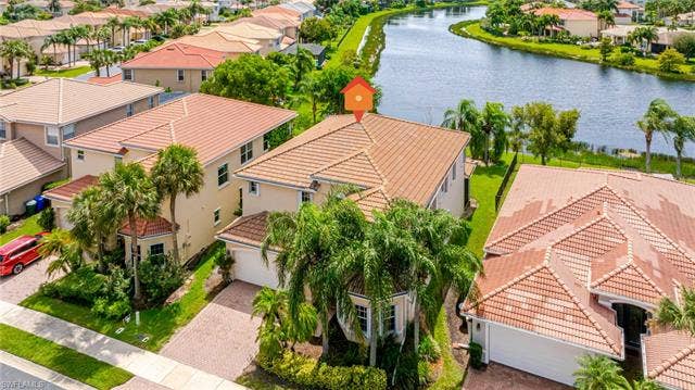 10310 Carolina Willow Dr, Fort Myers, FL 33913 Property featuring a tile roof, paved driveway, mature palm trees, and a waterside location with a manicured lawn