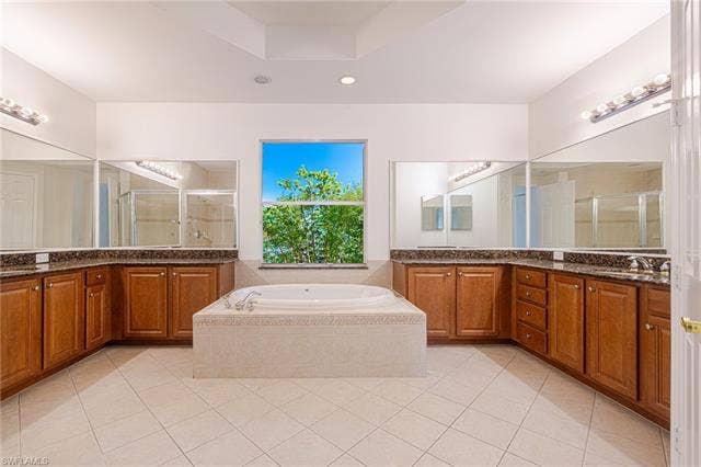 10310 Carolina Willow Dr, Fort Myers, FL 33913 Soaking tub with tiled surround, wood-finish cabinetry, dark stone countertops, large window, and wall-mounted mirrors