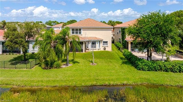 10310 Carolina Willow Dr, Fort Myers, FL 33913 Rear exterior featuring a covered patio, terraced landscaping, and a manicured lawn