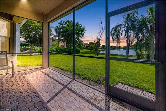 10310 Carolina Willow Dr, Fort Myers, FL 33913 Screened lanai featuring brick paver flooring, a manicured lawn, and a serene lake backdrop