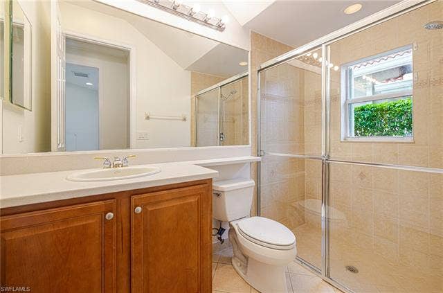 10310 Carolina Willow Dr, Fort Myers, FL 33913 Bathroom featuring a wood-finish vanity, light-toned countertop with an integrated sink, and a glass-enclosed shower with tiled walls