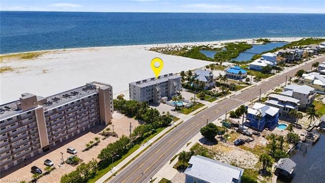 8300 Estero Blvd, #104, Fort Myers Beach, FL 33931 Beachfront condominium with direct beach access, featuring an exterior swimming pool, and a paved parking area - Virtually Edited Image