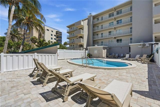 8300 Estero Blvd, #104, Fort Myers Beach, FL 33931 Outdoor swimming pool with integrated steps, surrounded by a paver patio and white privacy fencing - Virtually Edited Image