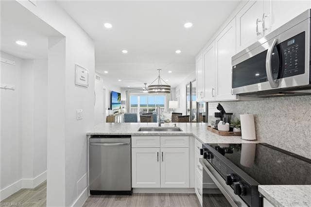 8300 Estero Blvd, #104, Fort Myers Beach, FL 33931 Modern kitchen featuring white shaker cabinetry, stainless steel appliances, light-toned countertops, and wood-finish flooring - Virtually Edited Image