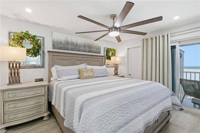8300 Estero Blvd, #104, Fort Myers Beach, FL 33931 Tray ceiling with recessed lighting, wood-finish flooring, wood-paneled headboard, ceiling fan with integrated lighting, and a glass sliding door leading to an outdoor balcony - Virtually Edited Image